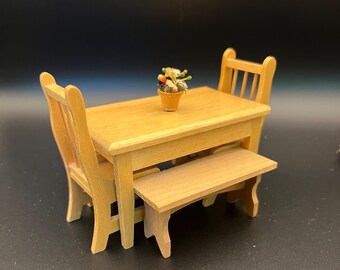 May include: A miniature wooden dining set with a table, two chairs, and a bench. A small pot of miniature vegetables sits on the table. The set is made of light-colored wood.