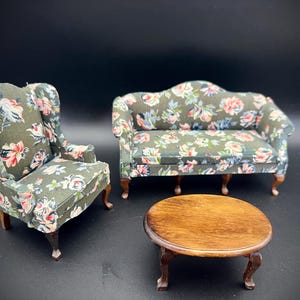 May include: Miniature dollhouse furniture set featuring a wingback chair, a loveseat, and a round coffee table. The furniture is upholstered in a floral pattern with pink, white, and blue flowers on a green background. The table and chair legs are brown.