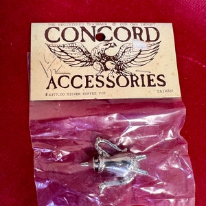 May include: A silver miniature coffee pot in a plastic bag with a label that reads "CONCORD ACCESSORIES #4277.00 SILVER COFFEE POT TAIWAN".