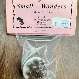 May include: A miniature item in a clear plastic bag, with a pink tag that reads "Small Wonders Made in U.S.A." and "For the Discriminating Miniature Collector." The item appears to be a small, white disc with brown and black pieces.