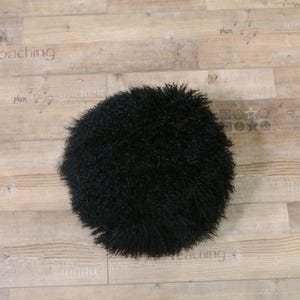 May include: A black fluffy round sheepskin rug. The rug is on a wooden floor.