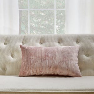 Peut inclure: Un coussin de canapé rose à motif géométrique avec un léger brillant. Le coussin est sur un canapé blanc capitonné.