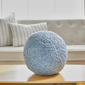 May include: A light blue round throw pillow with a fuzzy texture. The pillow is sitting on a wooden table.