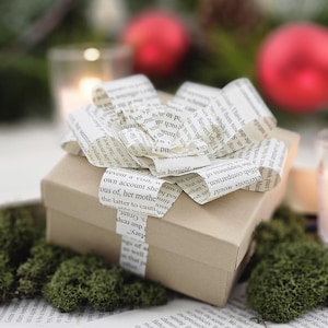 May include: A brown gift box wrapped with a bow made from pages of a book. The bow is tied in a knot and the ends of the pages are curled.