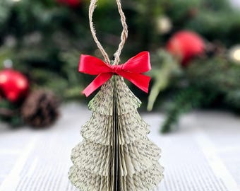 May include: A handmade Christmas tree ornament made from pages of a book, with a red ribbon bow. The ornament is shaped like a Christmas tree and is made from the pages of a book. The ornament is hanging from a twine loop.