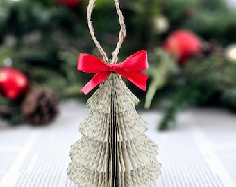May include: A handmade Christmas tree ornament made from pages of a book, with a red ribbon bow. The ornament is shaped like a Christmas tree and is made from the pages of a book. The ornament is hanging from a twine loop.