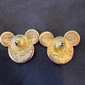 Pu&ograve; includere: Un paio di orecchini a bottone di Topolino dorati. Gli orecchini hanno la forma della testa di Topolino, con un viso rotondo e due orecchie rotonde. I retro hanno un perno e un supporto in plastica.