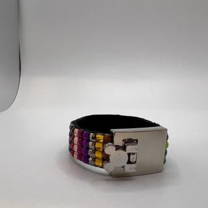Puede incluir: Una pulsera ancha de cuero negro con filas de cuentas de colores rosa, morado, amarillo y verde. La pulsera tiene un cierre plateado con un dise&ntilde;o de Mickey Mouse.