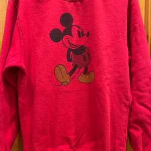 May include: Red sweatshirt with a vintage Mickey Mouse graphic. The sweatshirt has a crew neck and long sleeves.