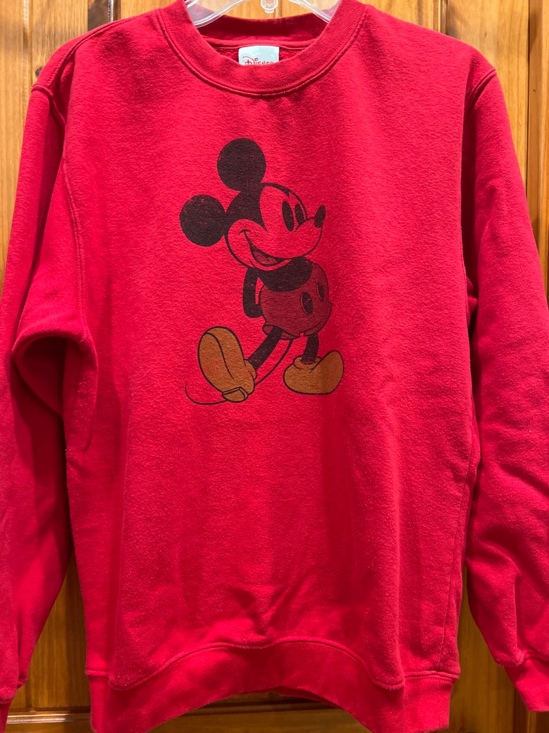 May include: Red sweatshirt with a vintage Mickey Mouse graphic. The sweatshirt has a crew neck and long sleeves.