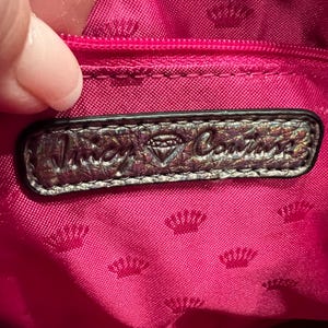 May include: A close-up of the inside of a pink handbag with a silver metallic label that reads "Juicy Couture" with a diamond logo.
