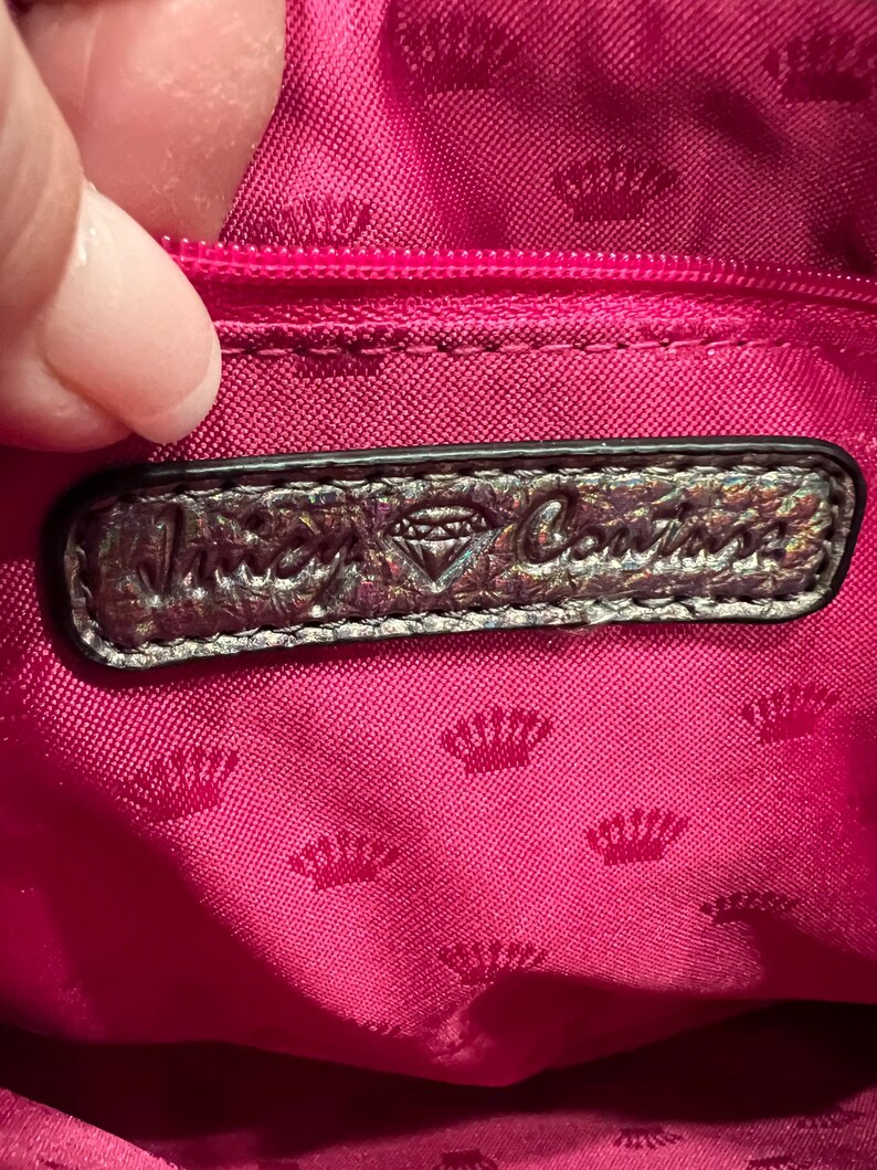 May include: A close-up of the inside of a pink handbag with a silver metallic label that reads "Juicy Couture" with a diamond logo.