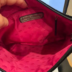May include: The inside of a black purse with a pink lining. The lining has a repeating pattern of crowns. The purse has a silver tag that says "Juicy Couture".