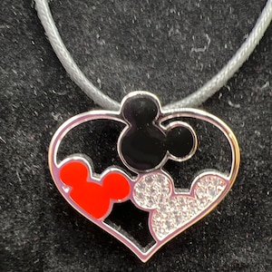 Puede incluir: Un collar con un colgante en forma de coraz&oacute;n plateado con tres cabezas de Mickey Mouse. Las cabezas de Mickey Mouse son negras, rojas y transparentes con diamantes de imitaci&oacute;n.