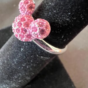 May include: A silver ring with a pink crystal design. The ring features three spherical shapes, with the largest at the base and two smaller ones above. This distinctive ring is a stylish accessory, perfect for adding a touch of sparkle.