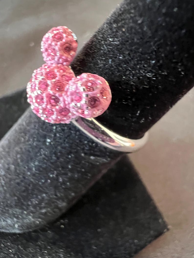 May include: A silver ring with a pink crystal design. The ring features three spherical shapes, with the largest at the base and two smaller ones above. This distinctive ring is a stylish accessory, perfect for adding a touch of sparkle.