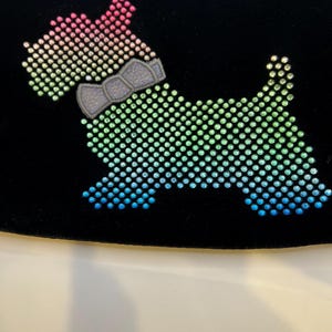 May include: A black velvet pouch with a rainbow-colored rhinestone dog design. The dog is wearing a gray bow tie.