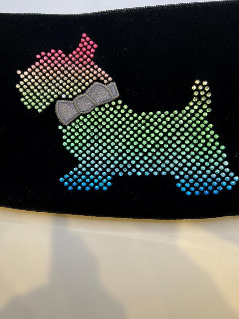 May include: A black velvet pouch with a rainbow-colored rhinestone dog design. The dog is wearing a gray bow tie.