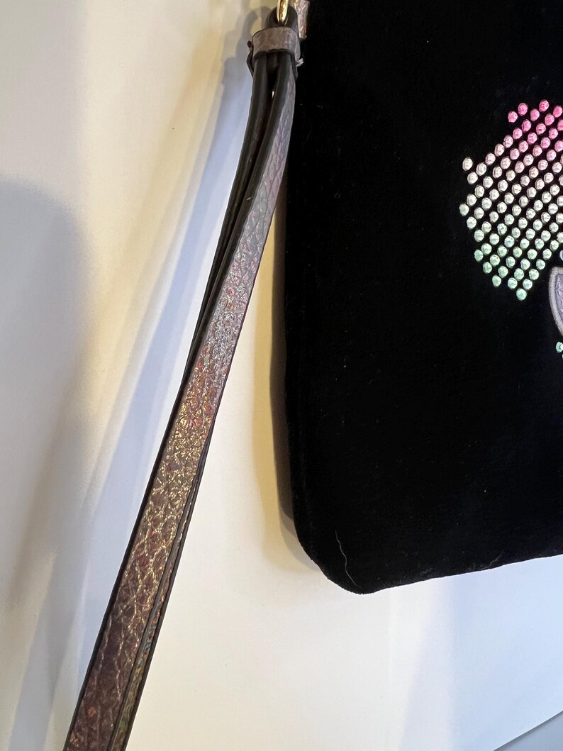 May include: A black velvet clutch bag with a rainbow-colored rhinestone design. The bag has a long, adjustable strap.
