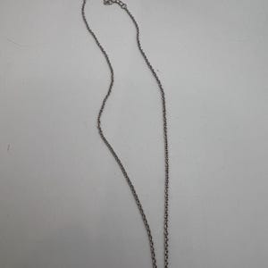 K&ouml;nnte beinhalten: Eine silberfarbene Halskette mit feiner Kette und kleinem Verschluss. Die Kette wird vor einem wei&szlig;en Hintergrund pr&auml;sentiert, um ihr schlichtes Design hervorzuheben. Die Kette ist etwa 45 cm lang.