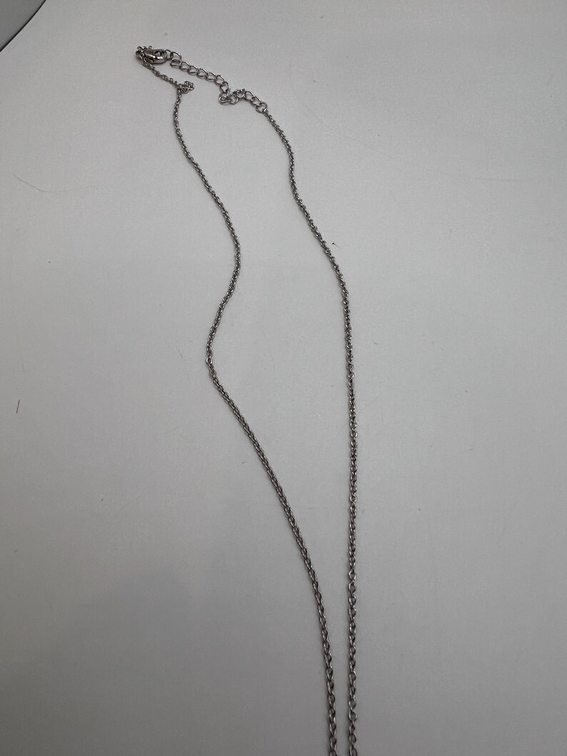 K&ouml;nnte beinhalten: Eine silberfarbene Halskette mit feiner Kette und kleinem Verschluss. Die Kette wird vor einem wei&szlig;en Hintergrund pr&auml;sentiert, um ihr schlichtes Design hervorzuheben. Die Kette ist etwa 45 cm lang.