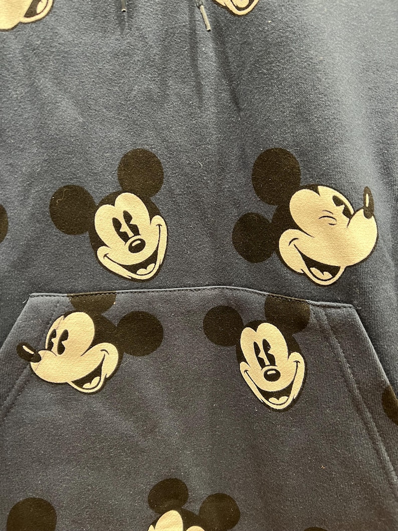 Pu&ograve; includere: Una felpa blu con un motivo ripetitivo di volti di Topolino. La felpa ha una tasca a marsupio.