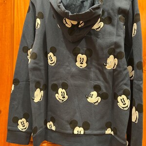 Pu&ograve; includere: Una felpa con cappuccio blu navy con un motivo ripetitivo di volti di Topolino.