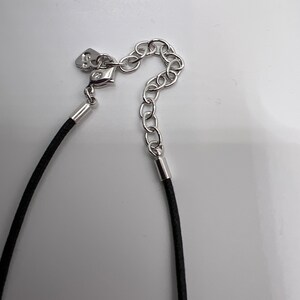 Puede incluir: Un collar de cord&oacute;n negro con un cierre y un extensor de cadena plateados.