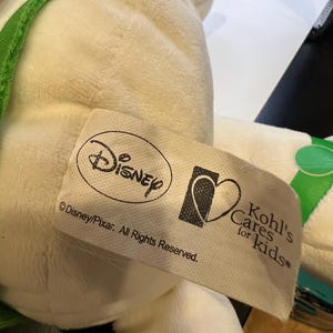 May include: White plush toy with green accents. The toy has a tag that reads "Disney/Pixar. All Rights Reserved." and a Kohl's Cares for Kids logo.