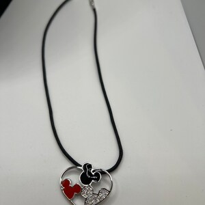 Puede incluir: Un collar de cord&oacute;n negro con un colgante de coraz&oacute;n plateado con un dise&ntilde;o de Mickey Mouse rojo y negro con pedrer&iacute;a.