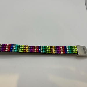 Puede incluir: Una pulsera colorida con un arco&iacute;ris de piedras preciosas. La pulsera presenta un cierre plateado y est&aacute; hecha de filas de piedras vibrantes y brillantes en varios colores, incluyendo rojo, verde, azul y amarillo.