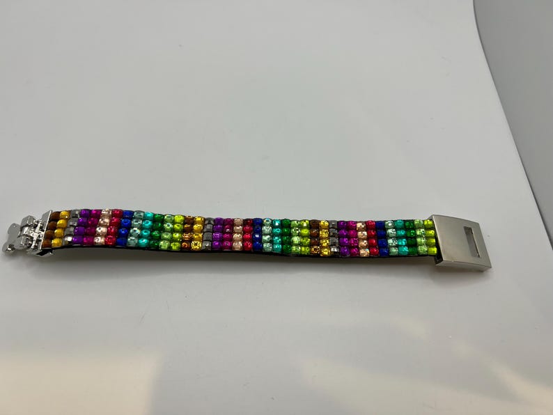 Puede incluir: Una pulsera colorida con un arco&iacute;ris de piedras preciosas. La pulsera presenta un cierre plateado y est&aacute; hecha de filas de piedras vibrantes y brillantes en varios colores, incluyendo rojo, verde, azul y amarillo.