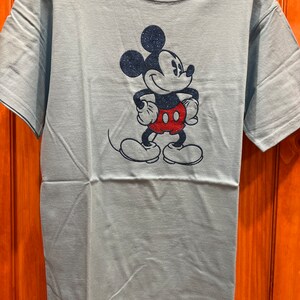 May include: A light blue t-shirt with a glittery blue and red Mickey Mouse graphic.