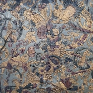 May include: A close-up of a blue and gold fabric with a floral pattern. The fabric is torn in the center, revealing the wood underneath.