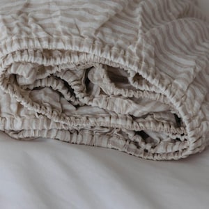 May include: A close-up of a beige and white striped fitted sheet, rolled up and folded on a white surface.