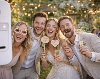 May include: Four smiling people pose for a photo, holding props at an outdoor event. One person wears diamond-shaped glasses, while others hold signs that read "Team" and "Party Crasher." The background features soft lighting.