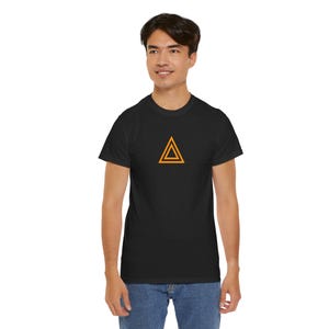 May include: Black t-shirt featuring a gold double triangle design. The shirt is made of a soft, comfortable material. The design is centered on the chest. The model is wearing blue jeans.