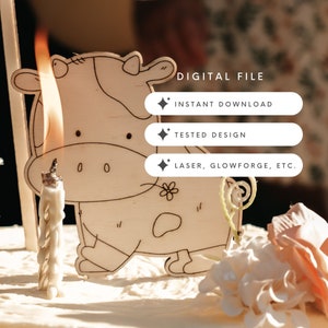 Puede incluir: Un adorno para pastel de madera en forma de vaca con una flor y un diseño de espiral. La vaca es blanca con manchas negras y tiene una vela delante. El texto "DIGITAL FILE", "INSTANT DOWNLOAD", "TESTED DESIGN" y "LASER, GLOWFORGE, ETC." es visible en la imagen.