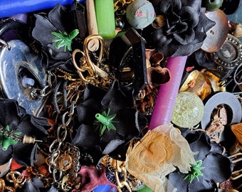 May include: A close-up of a collection of assorted trinkets and jewelry, including black fabric flowers, green plastic leaves, gold chains, purple and blue candles, a dice with the number 100, and a variety of other objects.