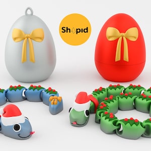 May include: A seasonal image showing two egg-shaped decorations, one silver and one red, each with a gold bow. Below, a blue and red snake toy and a green wreath toy, both wearing Santa hats, create a cheerful Christmas theme.