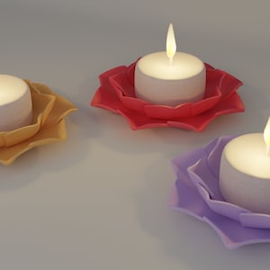 Może przedstawiać: Trzy tealighty w świecznikach w kształcie lotosu. Świeczniki są żółte, czerwone i fioletowe.