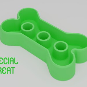 May include: Green plastic bone-shaped dog treat dispenser with three holes. The dispenser has the words "SPECIAL TREAT" printed on the front.