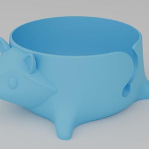 May include: A light blue yarn bowl shaped like a stylized hedgehog with a smooth matte finish. The bowl features a circular opening at the top and a J-shaped cutout on the side for yarn to pass through. A yellow circular logo with the text Shpid is visible.