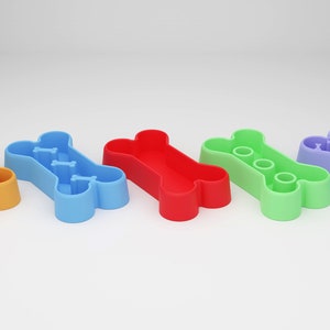 May include: Five bone-shaped dog bowls in different colors: orange, blue, red, green, and purple. Each bowl has a different pattern inside.