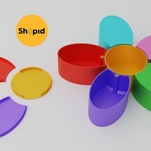 May include: A colorful flower-shaped container with six compartments, each a different color: red, orange, yellow, green, blue, and pink. The lid is yellow and the container is open, revealing the compartments.
