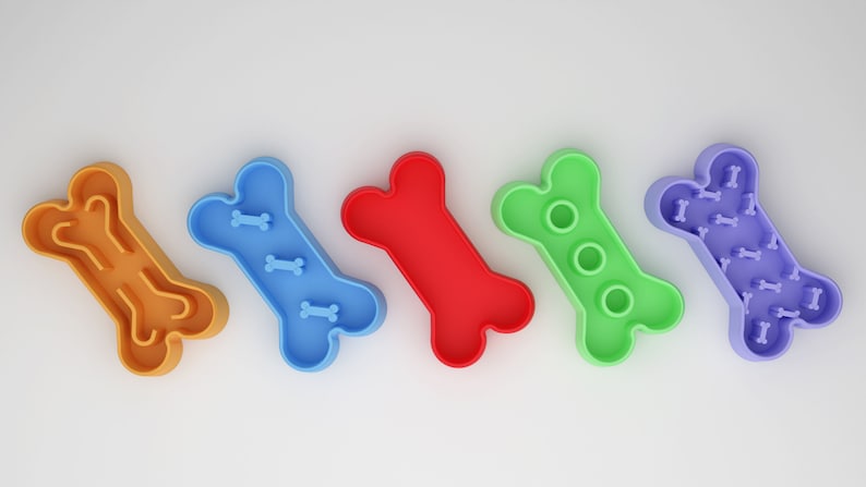 May include: Five dog bone shaped slow feeder bowls in different colors: orange, blue, red, green, and purple. Each bowl has a different design of raised bumps and ridges to slow down eating.