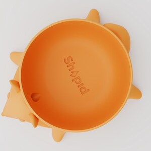 May include: An orange silicone bowl shaped like a hedgehog, featuring the embossed text "Shapid" in the center. The bowl has small, rounded protrusions along the sides representing the hedgehog's spikes, and a small circular hole near the bottom rim.