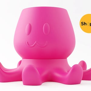 Puede incluir: Una maceta rosa brillante con forma de pulpo con una cara sonriente y tentáculos redondeados. La maceta tiene una abertura cilíndrica en la parte superior para las plantas. La palabra "Shopid" está en un círculo amarillo.