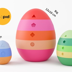 May include: Three colorful, egg-shaped objects in varying sizes. The largest is 12x10 cm, the medium is 7x6 cm, and the smallest is a 5x4 cm keychain. The eggs are striped with different colors and have geometric cutouts. The logo "Shopid" is in the upper left.