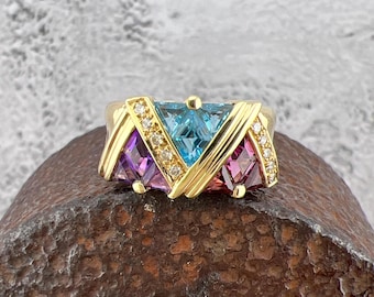 May include: A gold ring with a triangular design featuring blue, purple, and pink gemstones. The ring is set with small diamonds around the gemstones.